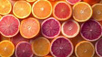 Fresh orange and blood orange citrus fruit slices arranged in rows showing vibrant pink, red and orange flesh colors, creating natural pattern background.