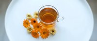 Herbal tea with dried chamomile and calendula flowers on white plate, overhead view for wellness and natural beverage design projects.