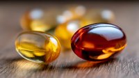 Colorful vitamin supplement capsules with omega-3 fish oil and vitamin D in soft gel form on wooden surface with natural lighting and shallow depth of field.