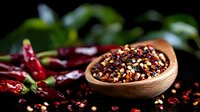 Mixed peppercorns in wooden bowl with red chili peppers on dark background, aromatic spices and seasonings for cooking and food preparation.