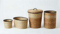 Set of four woven storage baskets in natural tones with dark trim, ranging from small to large sizes including lidded hamper for home organization.