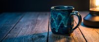 Blue ceramic coffee mug with marbled pattern on rustic wooden table in warm ambient lighting for cozy morning beverage moments and kitchen decor.