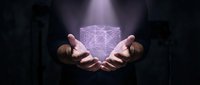 Young man with brown skin tone holding glowing geometric wireframe cube in cupped hands against dark background, representing technology, innovation, data science, and digital transformation concepts.