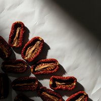 Dried red chili peppers cut in half showing seeds and interior texture with dramatic lighting and shadows on textured white surface for culinary content.