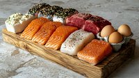 Fresh protein assortment on wooden board with raw salmon, tuna, beef, chicken, and eggs for healthy cooking and meal preparation.