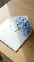 Blue hydrangea flower on white envelope placed on wooden table surface for romantic correspondence and greeting card concepts.