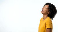 Young man with dark curly hair and medium brown skin tone wearing bright yellow t-shirt, looking upward with positive expression against white background for portrait and lifestyle use.