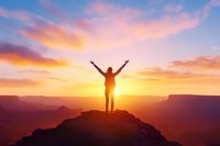 Silhouette of person with raised arms standing on mountain peak against dramatic sunset sky and canyon landscape, expressing freedom and achievement.