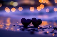 Two black hearts on wet pavement with warm bokeh lights creating romantic evening atmosphere for Valentine's Day and love concepts.