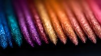 Macro shot of metallic colored pencils in vibrant blue, purple, gold and copper tones showing glittery texture detail arranged in diagonal line on dark background.