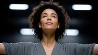 Young African American woman with curly hair stretching arms wide in modern gym, expressing freedom and achievement after successful workout session.