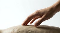 Male hand gently touching soft beige fabric surface in minimalist composition for textile and comfort concepts.
