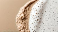 Close-up of creamy coffee foam with rich bubbles and texture, showing barista art detail for beverage and cafe marketing materials.