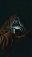 Young woman using smartphone under blanket in dark room with glowing screen light creating cozy nighttime atmosphere for social media and technology concepts.