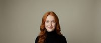 Professional redhead woman in black turtleneck sweater smiling confidently against neutral background for business and corporate marketing materials.