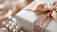 Elegant white gift box decorated with delicate lace trim, peach satin ribbon bow and pearl embellishments against soft blurred background for wedding or celebration.