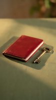 Vintage burgundy leather journal with antique brass key on neutral fabric surface, symbolizing secrets, memories, and personal reflection for editorial and lifestyle projects.
