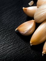 Fresh garlic cloves arranged on dark slate background with dramatic lighting and selective focus, creating contrast between light ingredients and dark surface.