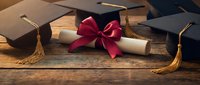 Graduation caps with diploma tied with red ribbon on wooden background representing academic achievement and educational success ceremony.