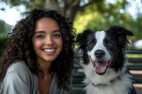 Young Hispanic woman with curly dark hair smiling outdoors with happy Border Collie dog in park setting. Natural daylight portrait showing joyful connection between pet and owner.