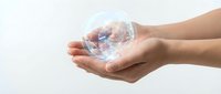 Hands gently holding transparent glass sphere with rainbow light reflections on clean white background for environmental and sustainability concepts.