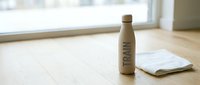 Insulated stainless steel water bottle with train text on wooden floor next to notebook, promoting eco-friendly hydration and sustainable lifestyle choices.
