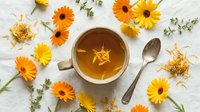 Herbal tea with chamomile and gerbera flowers arranged on white marble surface, flat lay composition for wellness and natural beverage design projects.