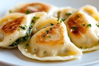 Pan-fried dumplings garnished with fresh herbs on white plate, golden-brown crispy bottom and tender wrapper filled with savory mixture.
