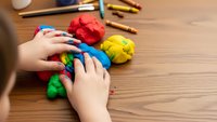 Child hands playing with colorful modeling clay on wooden table. Creative arts and crafts activity for kids development and learning through play.