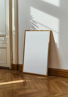 Blank white poster mockup with wooden frame leaning on wall, natural window shadows and palm leaves reflection on bright interior with parquet floor.