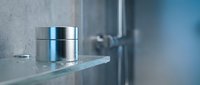 Stainless steel container on glass shelf in modern bathroom with blurred fixtures and neutral tones for storage and organization.