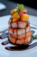 Stacked grilled shrimp with mango cubes and balsamic reduction sauce on white plate, garnished with fresh herbs and radish. Gourmet seafood appetizer.