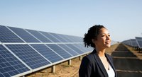 Woman professional standing in front of solar panels at renewable energy farm. Female engineer or technician inspecting sustainable power generation facility for clean energy business use.