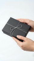 Hands holding elegant black gift box with silver ribbon bow on white background for special occasions and celebrations.