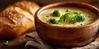 Creamy broccoli soup in rustic wooden bowl with fresh herbs and crusty bread, comfort food for cold weather dining and healthy meal preparation.
