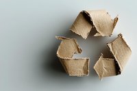 Recycling symbol made from torn brown cardboard pieces arranged on light background, representing environmental sustainability and waste reduction.