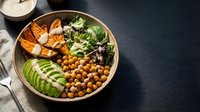 Healthy Buddha bowl with roasted chickpeas, sliced avocado, sweet potato, mixed greens and tahini dressing on dark background for nutritious meal planning.