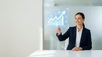 Businesswoman in dark blazer and white shirt pointing at glowing growth chart with upward arrow and financial icons on glass screen, representing business success and data analysis.