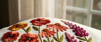 Colorful embroidered flowers on white fabric featuring orange daisies and purple blooms. Handcrafted needlework art for textile and craft projects.