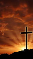 Dramatic cross silhouette against fiery orange sunset sky with storm clouds for religious and spiritual themes.
