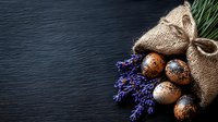 Rustic Easter eggs with lavender flowers spilling from burlap sack on dark wooden background for spring holiday decorating and natural craft projects.
