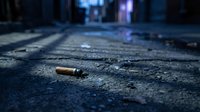 Cigarette butt discarded on a dark urban alley pavement at night, highlighting pollution and street neglect concepts.
