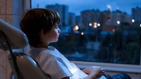 Young professional man relaxing in modern office chair looking out window at evening city skyline with glowing lights creating peaceful work-life balance moment.