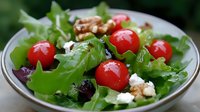 Fresh mixed green salad with cherry tomatoes, feta cheese crumbles, walnuts and olives in ceramic bowl, close up view on natural background.