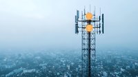 Telecommunication tower with cellular antennas and signal transmitters against foggy urban cityscape background in blue morning atmosphere.