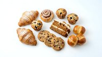Assorted fresh baked goods including croissants, muffins, and cookies arranged on white background for bakery, cafe, or food business marketing materials.