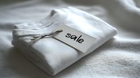 Neatly folded white t-shirts with sale tag attached by string, displayed on soft white textile background for retail promotion.