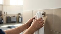 Mechanic drying dirty hands with white towel on wall-mounted holder in auto repair shop, emphasizing hygiene and cleanliness after work.