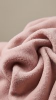Soft pink fleece fabric with flowing folds and gentle curves creating cozy textile texture for home decor and fashion design projects.