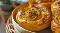 Fresh baked spiral sweet buns with herbs and sesame seeds, golden brown crust and glossy surface, close up view of homemade pastry on wooden background.